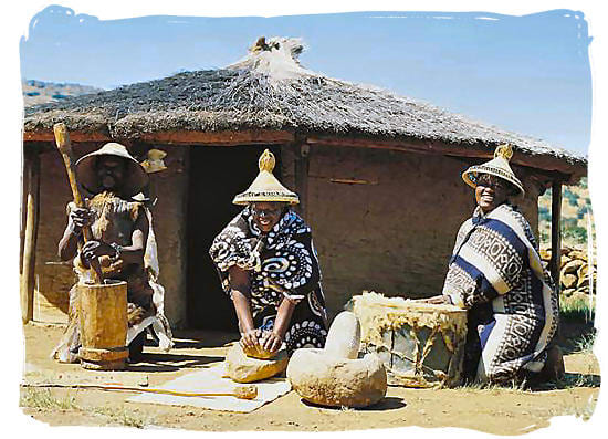 Basotho People next to their hut and adorned in their traditional garb(Their hats are called ("Modianyeho")