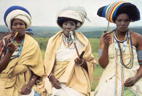 Xhosa Women in their traditional garb and smoking their pipes. The elegant beadwork on their pipes keeps the pipestems cool enough to handle