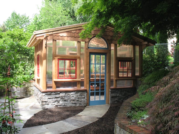 beautiful wood garden shed with walls of windows including arched window lights and a stone foundation