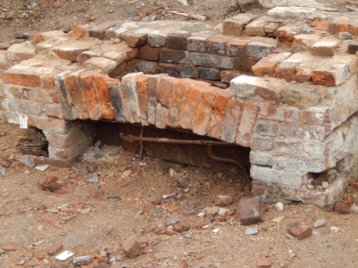 A hearth in a cellar sticks out just above the backfill, still complete with its hooks from which cooking pots would be hung.