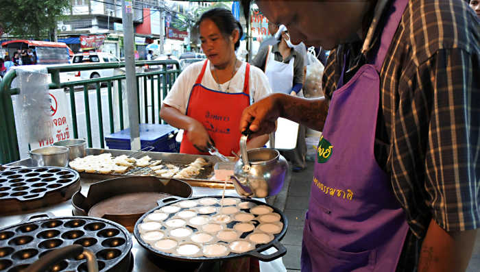 The preparation of the sweet coconut dessert 'khanom krok'. Here a vendor pours the coconut milk filling into cup-cake shaped moulds
