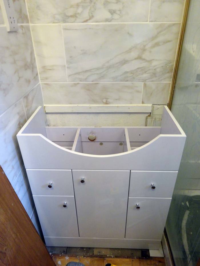 Installing the new vanity unit 5 inches forward of the back wall to allow water and waste pipes to be behind the cupboard, rather than inside.