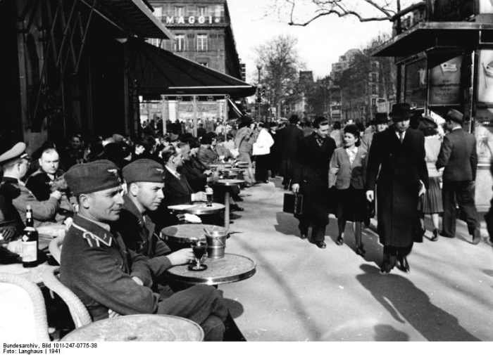 German soldiers and officers mingling with French population on a sunny but still cold day of 1941. The cafe in this picture is most likely to be "Les Deux Magots" on Boulevard Saint- Germain