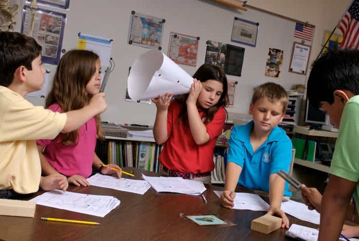 This group of students is employing several different learning methods at the same time: one student is writing, another is participating, another is watching, and another is listening to the results of the experiment.