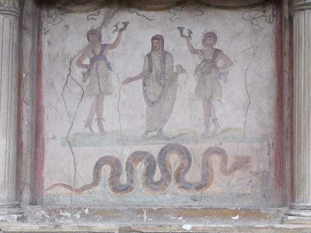 VI.15.1 Pompeii. December 2006. Household lararium in service area. Painting of serpent, (Agathodemone), garlands and three figures. The household gods (Lares) are either side of the guardian spirit (genius loci) of the house.