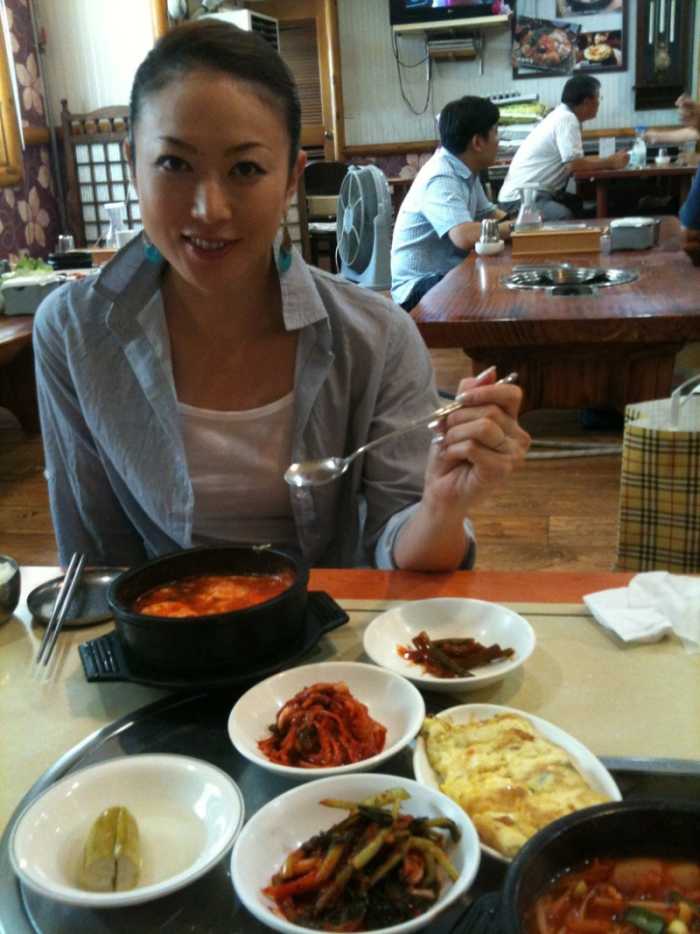 Masami Tanaka is enjoying a nice meal with many different foods on the table. She is about to have a spoonful of soup perhaps?