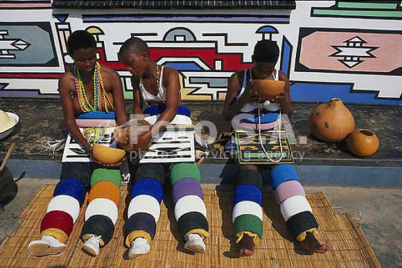 Ndebele girls in their traditional clothing and sitting next to their house they decorated themselves