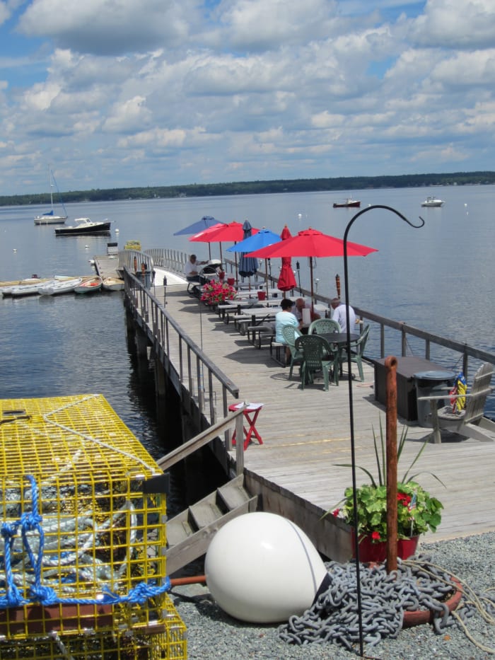 The Pier and picnic tables at Perry's Lobster Shack, Newbury Neck, Surry, ME with a view of the harbor and the mountains of Mount Desert Island and Acadia National Park in the distance