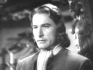 Errol Flynn's squarish face is made to look more even more square by the wavy, geometrical hairstyle that ends in both vertical and horizontal line with his chin.
