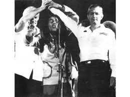 Bob Marley unite two warring factions JLP and PNP at his 1978 One Love Peace Concert. This is after they tried to kill him. Symbolic of uniting communism and capitalism.