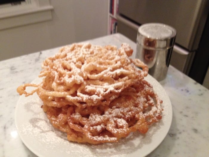 Allow your funnel cakes to cool slightly after removing them from the hot oil. Some of the oil will drain off and the funnel cake won't melt them powdered sugar.