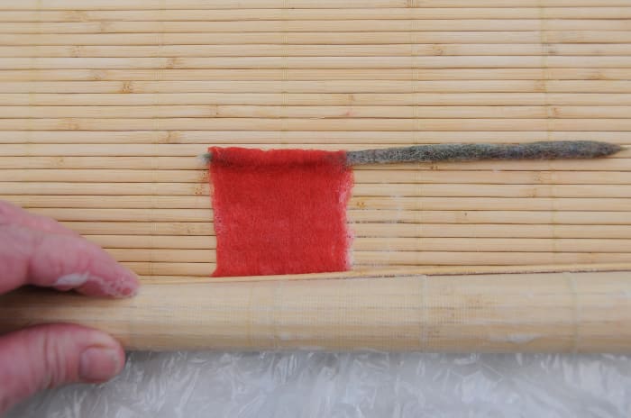 Roll the center bud of the rose inside the sushi mat, Include the pipe cleaner once the lower end has been felted.