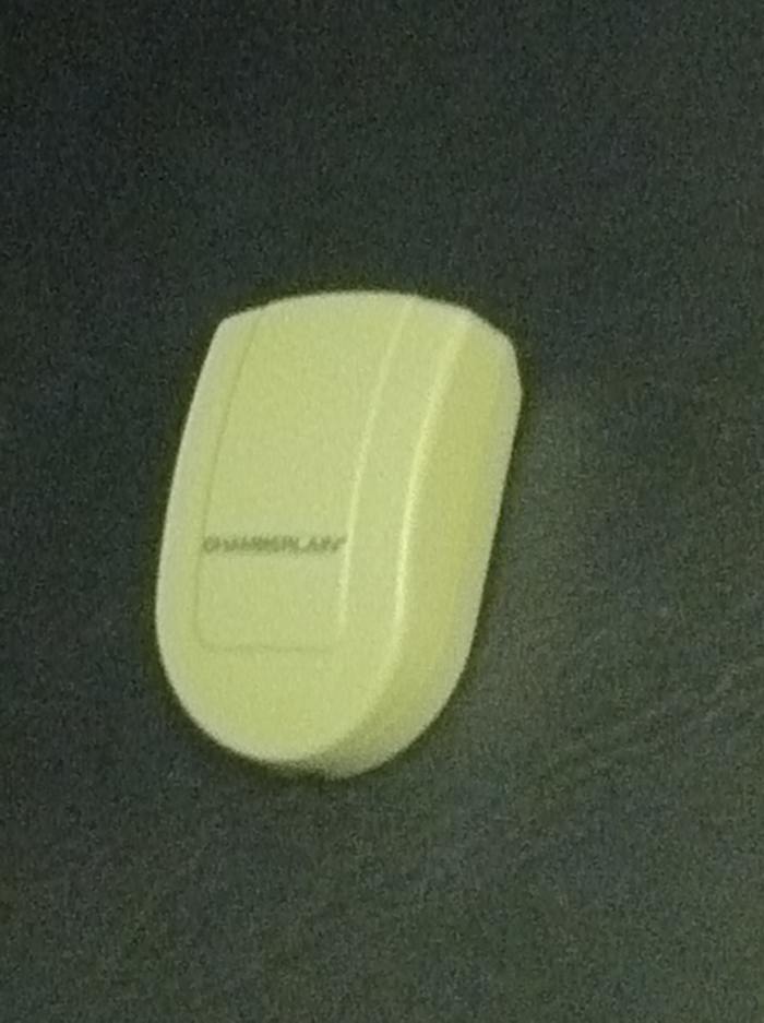 The sensor component attaches directly onto the garage door, signaling the receiver indoors whether the door is open (red light) or closed (green light).