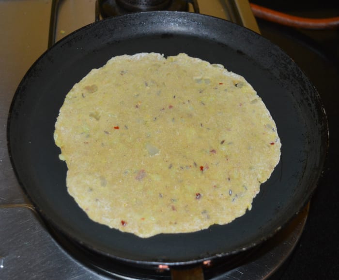Step three: Heat a griddle or flat pan. Add a few drops of oil or ghee. Place a raw paratha on it. Keep the heat at medium.