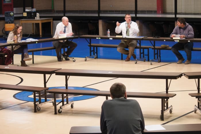 The woman to the left is showing she is timid and will be reluctant to speak up by keeping her left arm to her side and her right hand off the table, clutching the water bottle.