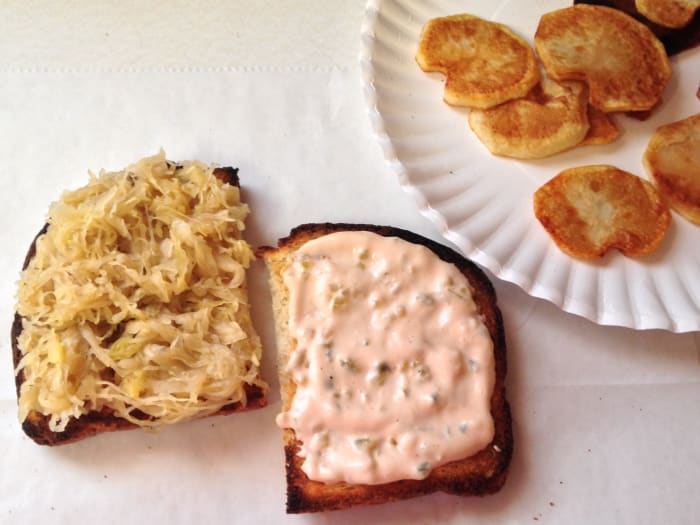 Constructing the veggie Reuben sandwich, with toasted bread, sauerkraut with crushed pineapple, fried potatoes, Thousand Island dressing.