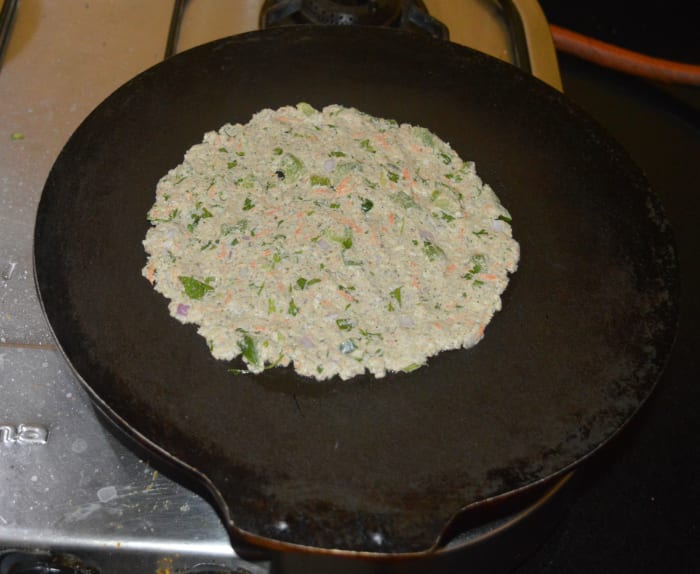 Step four: Grease a flat pan or griddle with some oil. Take a big lemon-sized portion of dough in your hand. Shape it like a ball. Place it on the pan. Pat it with wet fingers and extend the dough around evenly to get a 4 or 5-inch disc. Heat it.