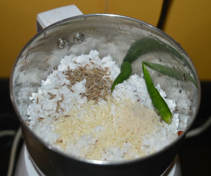 Step two: Make the gravy for the curry. Add grated coconut, cumin seeds, green chilies, hing powder, and raw rice to a mixer jar. Add water little by little and grind to get a smooth paste.