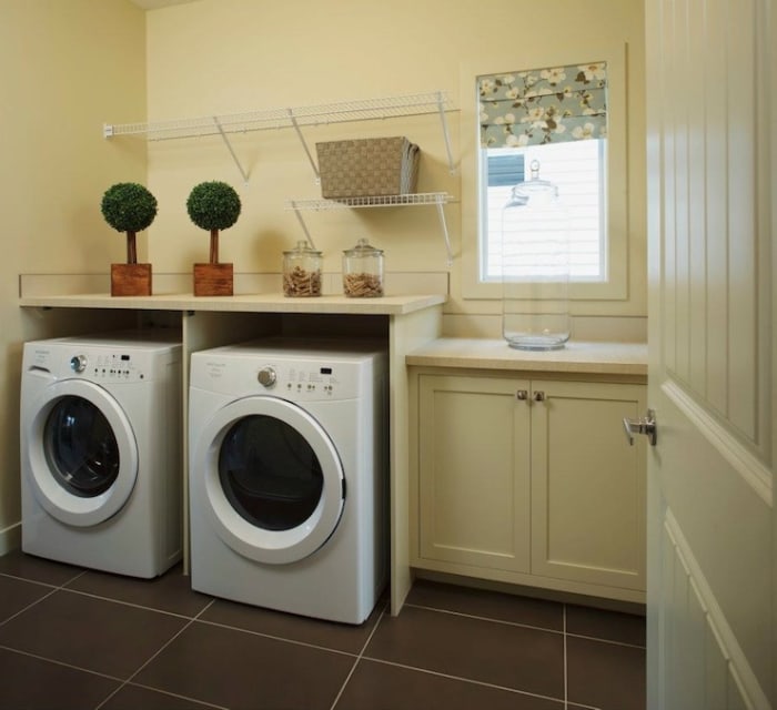 Lovely pale yellow laundry room with cream cabinetry with white laminate countertops and the white front-load washer and dryer.
