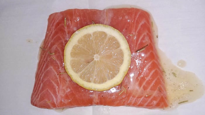 Glaze each salmon fillet with lemon butter sauce and then place a lemon slice on top. Now it's ready to bake.