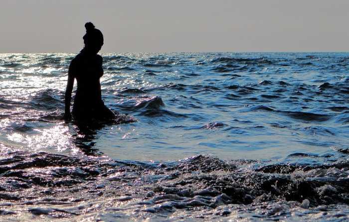A woman wades in the ocean's vast water as she contemplates.