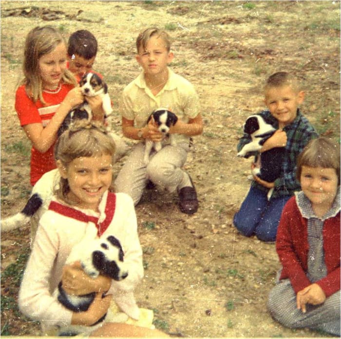 That's me, wearing a white sweater, on the front left holding a puppy. My sister who is five years younger than me is to the front right and not holding a puppy. My brother is behind her. The rest are friends.
