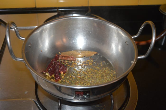 Step one: Heat oil in a deep-bottomed pan. Add the mustard seeds and allow them to crackle. Add fenugreek seeds, cumin seeds, fennel seeds, bay leaf, cinnamon stick, cloves, and broken red chilies. Saute on low heat for 30 seconds.