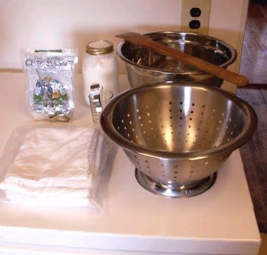 Basic supplies needed to make feta cheese: a large bowl and colander, a long spoon, large cotton tea towels, non-iodized salt, and yogurt or cultured buttermilk. Not shown is liquid vegetable rennet, or your choice of rennet.