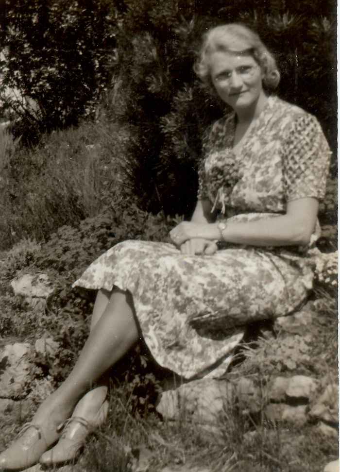 My paternal grandmother is sitting on a retaining wall of her rock garden going down to the lake.