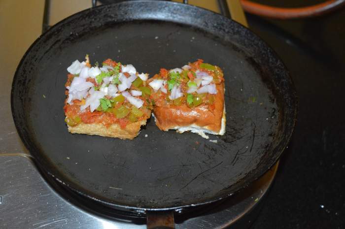 Reduce the heat. Generously top each piece with the masala. Garnish both the pieces with freshly chopped onions and coriander leaves. Place one piece above the other as shown here.