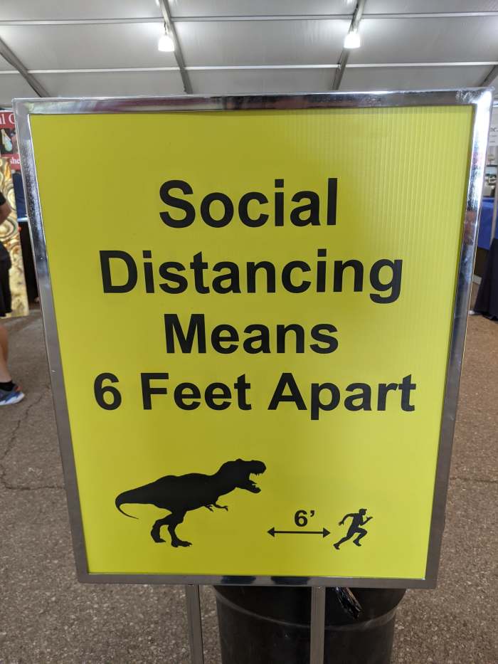 COVID Vaccine doesn't protect against a hungry dinosaur. - photo of social distancing poster at an event