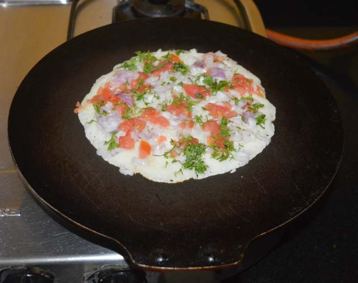 Step two: Heat a pan and grease it with some oil or ghee. Add a ladle full of the batter on it and spread it a little. Top the pancake with a mixture of chopped onions, ginger, tomatoes, green chilies, and coriander leaves.