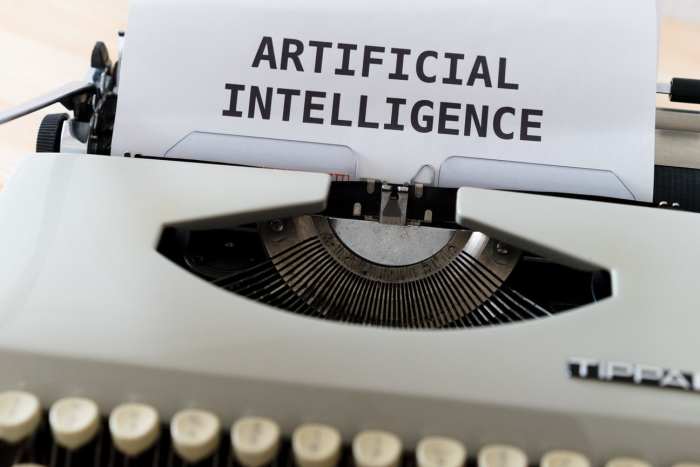 A black and white typewriter with printed artificial intelligence words on paper. Photo by Markus Winkler via Unsplash.