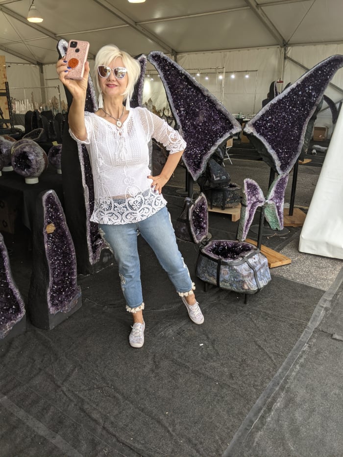 My at the annual Tucson Gem & Mineral Show taking a selfie in front of a room full of large geodes with amethyst crystals growing inside them
