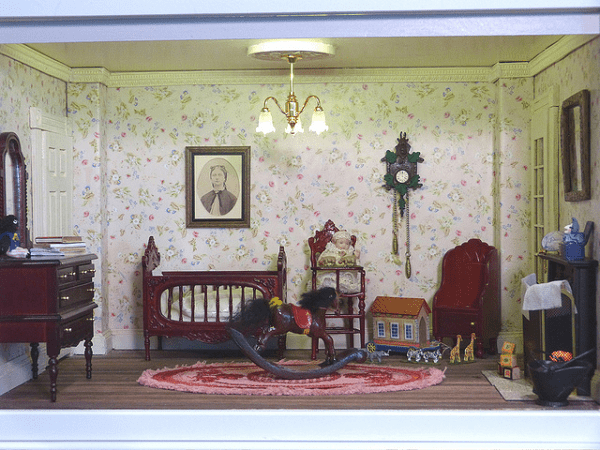 A miniature Victorian style nursery interior, Notice the furniture, little baby sitting on a high-chair, a crib, and a rocking horse.
