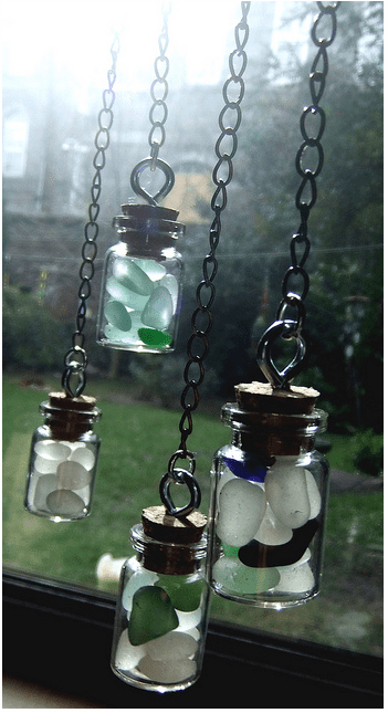 Pretty ornaments made by filling mini corked glass bottles with sea glass and hanging them from chain. Perfect for a window display.