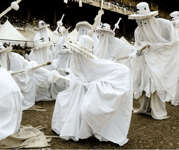 Eyo masquerades dancing to the beat of the drums, wearing the traditional all white regalia and wide-brimmed hats.