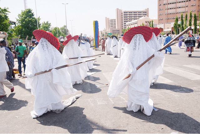The Eyo masquerade's costume is one of splendour. White flowing robes, lace veils, prominent hats (different groups wear different hats), and the famous Opambata, a long thick cane that's a part of the ensemble.