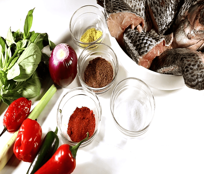 Clockwise from bottom to top – Red chilies, green bird’s eye chilies, scotch bonnet peppers, lemongrass, fresh bay leaf, red onion, spices and seasonings, and Tilapia fish