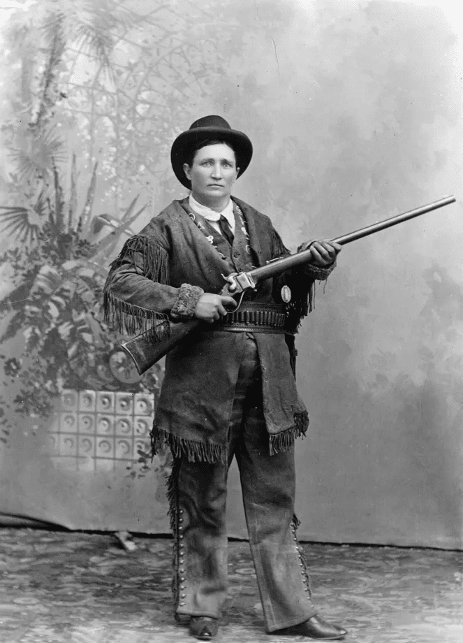 An early view of Calamity Jane wearing buckskins, with an ivory-gripped Colt Single Action Army revolver tucked in her hand-tooled holster, holding a Sharps rifle