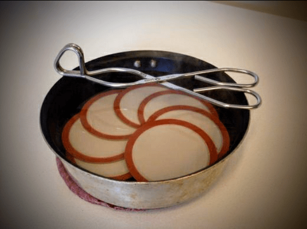 Either gently simmer the lids (don't boil!), or set them in a small pan and pour on boiling water to cover, to scald them.
