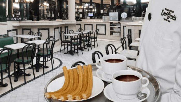 Inside view of El Café San Gines as a server, or un mesero, delivers a plate of churros con chocolate.