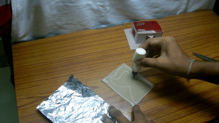 Start by cutting paper to make the roof. You need to keep in mind that the roof of the house should be bigger than its base. Then paste the plastic wrapper on the roof. The shiny surface should be on top.
