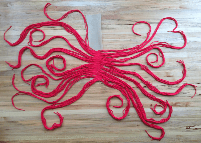  Ici, la moitié du fil a été attachée à la bande de tissu. Continuez jusqu'à ce que vous utilisiez tous les brins rouges.