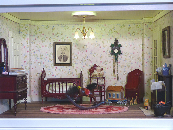 A miniature Victorian style nursery interior, Notice the furniture, little baby sitting on a high-chair, a crib, and a rocking horse.