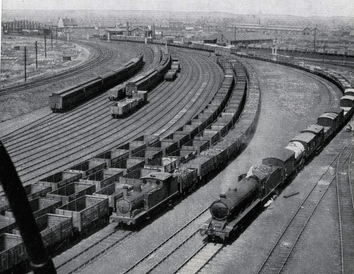 1941, private owner coal wagons lined up in sidings for war traffic. Due to the shortage of open wagon stock they would not only be used on coal trains. A very long mixed freight train rounds the curve on the right
