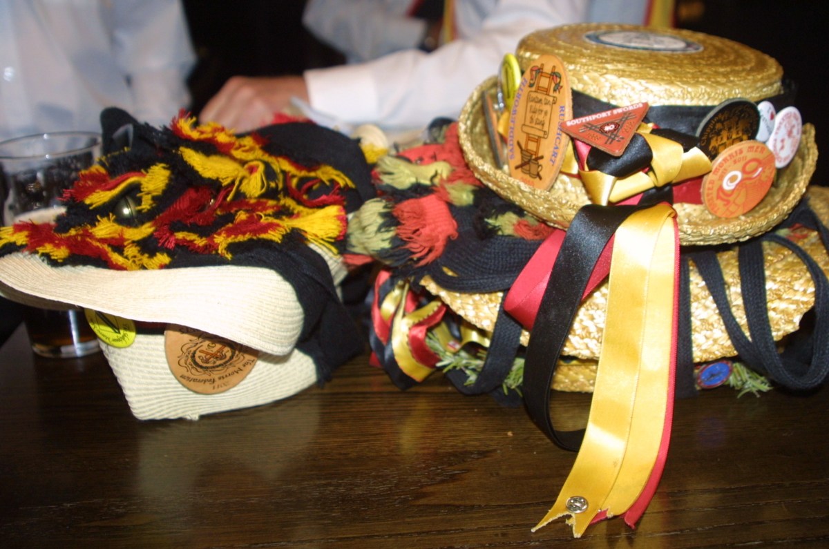 Morris dancers wear straw hats festooned with ribbons and badges from events they've attended.