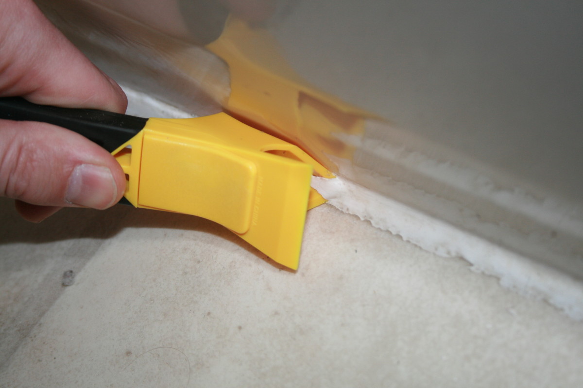 Inserting the pointed edge into the caulk with the edged bottom laying in the seam.