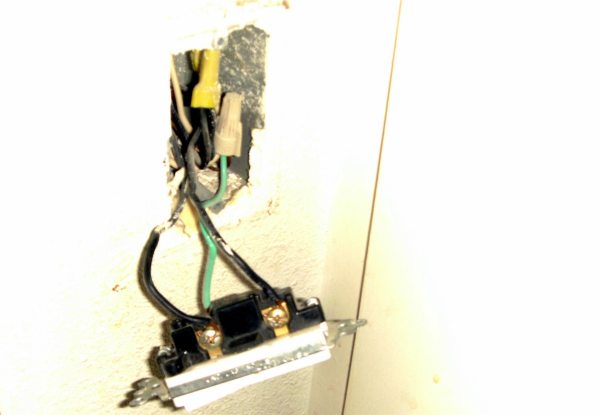 The switch has been pulled from the wall with the power turned off, exposing the wires and screws holding them.  The green ground wire goes to a green ground screw.
