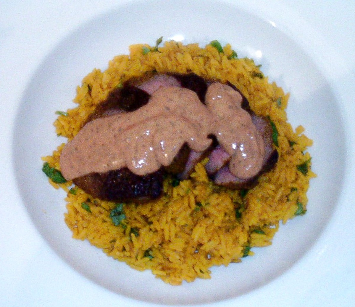Slices of curried ostrich fillet steak on turmeric rice with spicy sauce